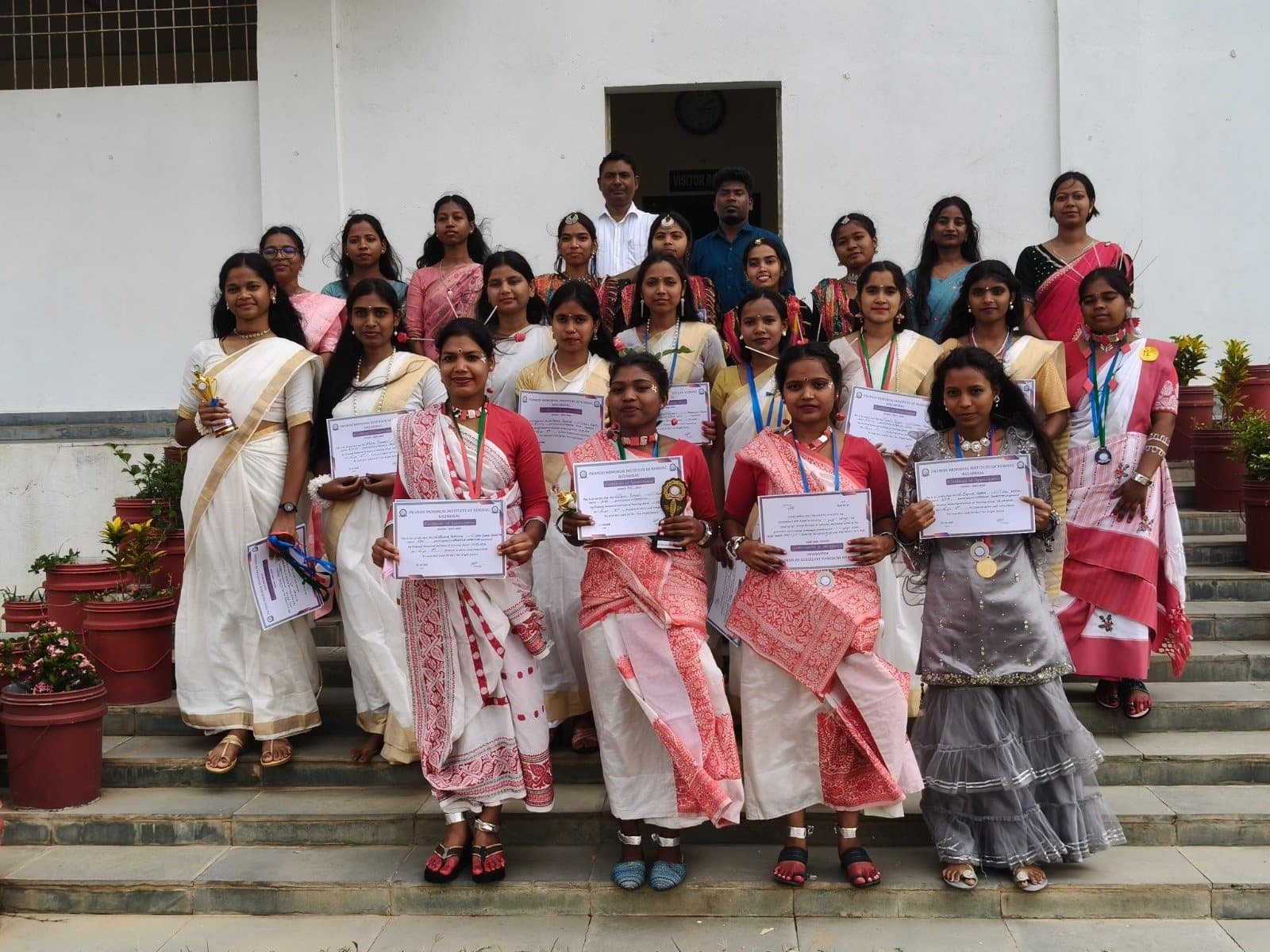 Prize winners in traditional dress with their certificates and trophies on the institute steps